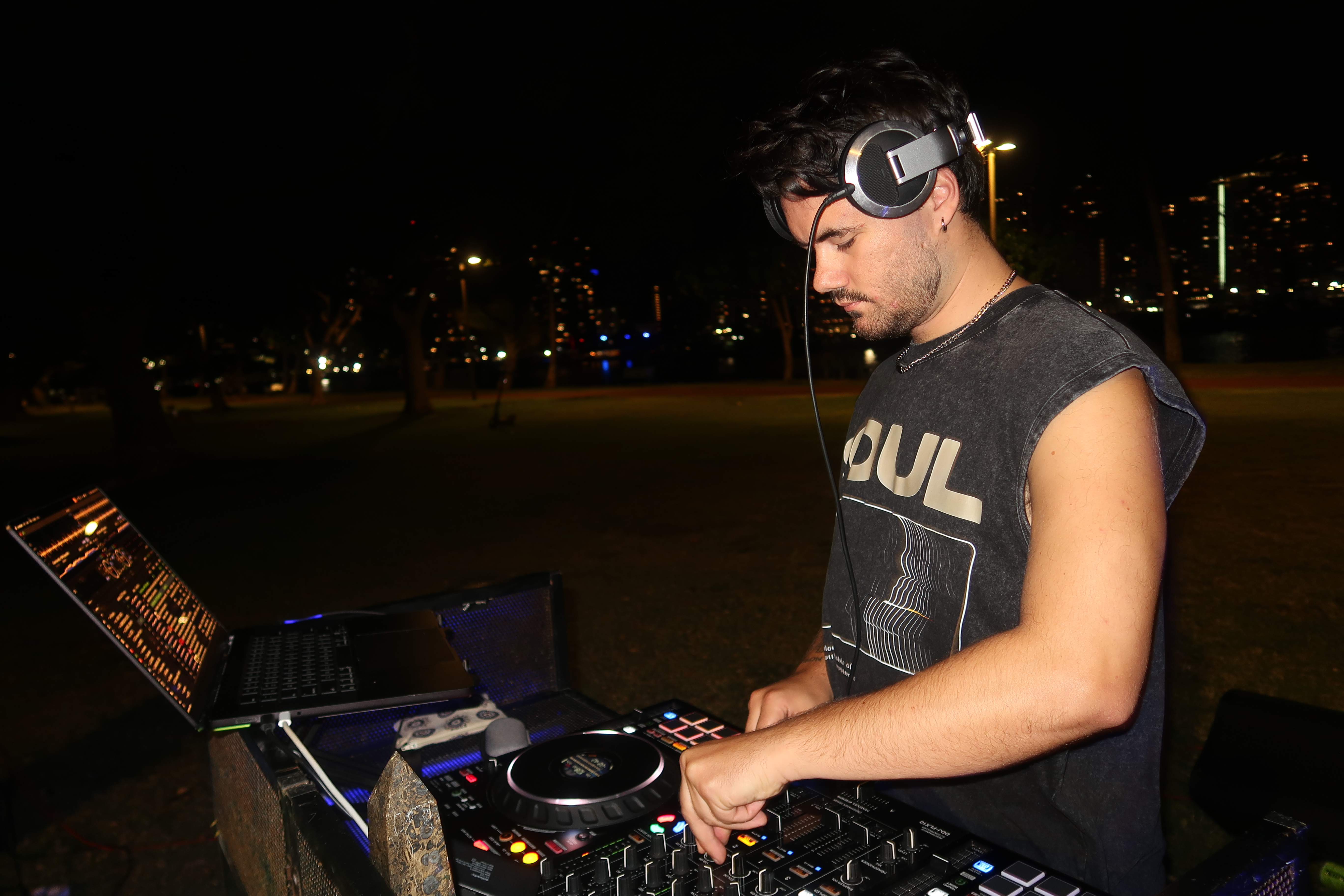 DJ at decks, city lights behind